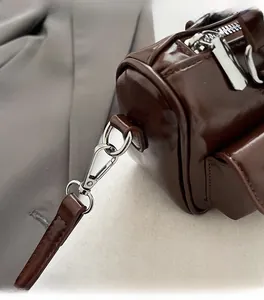 Detail of silver metal hooks and D-rings on dark brown glossy synthetic leather bag