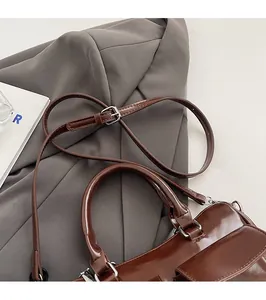 Detail of dark brown polished leather bag with silver hardware and adjustable strap