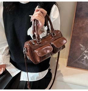 Detail of dark brown glossy barrel bag with dual front utility pockets and silver hardware
