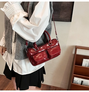 Detailed close-up of dark red glossy leather shoulder bag with dual front flap pockets