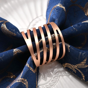 Elegant rose gold metal napkin ring with diagonal stripes on a dark blue napkin and white plate