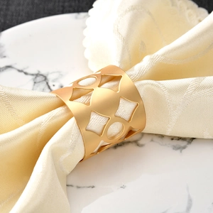 Elegant gold hollow napkin ring with raindrop pattern on white marble plate and beige napkin