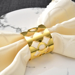 Golden plated hollow raindrop napkin ring on white napkin and marble plate background