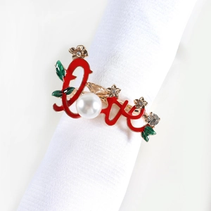 Macro shot of gold plated LOVE napkin ring with red enamel leaf and pearl detail