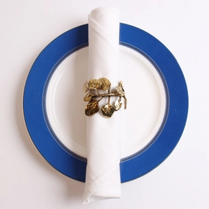 Detailed view of antique gold olive leaf napkin ring on a white fabric napkin and plate