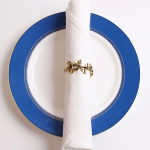 Detail view of a vintage gold olive branch napkin ring on a white napkin over a blue plate