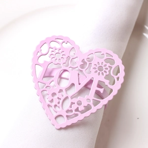 Macro shot of pink heart-shaped metal napkin ring featuring LOVE cutouts and floral patterns