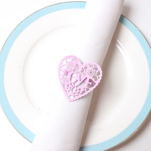 Close-up of pink heart-shaped napkin ring with laser-cut love text on white napkin