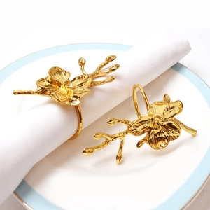 Elegant gold orchid flower napkin rings set on white linens for hotel table decor