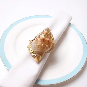 Macro detail of natural conch shell napkin ring with golden edges on white linen