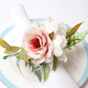 Pink rose floral napkin ring with greenery on a white napkin and ceramic plate