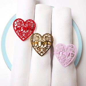 Close-up of heart-shaped LOVE cutout napkin rings in red gold and pink on white napkins