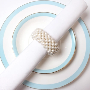 Elegant white pearl woven napkin ring displayed on a white fabric napkin and blue plate