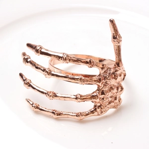 Rose gold skeleton hand napkin ring with realistic bone texture on a white ceramic plate