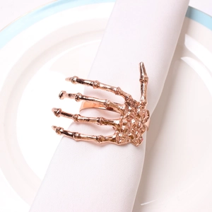 Detailed view of rose gold skeleton hand napkin ring on a white fabric napkin and ceramic plate