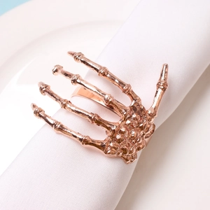 Detailed view of a rose gold skeleton hand napkin ring set on a white cloth for Halloween