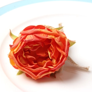 Orange fabric rose napkin ring with rustic jute twine on a white ceramic plate