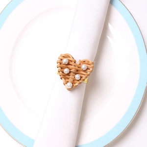 Detail of woven rattan heart napkin ring with pearls on a white linen napkin