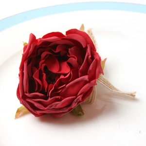 Realistic red fabric rose napkin ring with twine base on a ceramic plate, rustic style