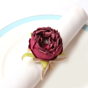 Close-up of a burgundy rose napkin ring with green leaves on a white fabric napkin