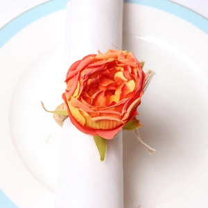 Detail of vibrant orange rose napkin ring with green leaves on a white ceramic plate