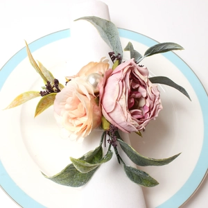 Detail eines rosa Rosen-Serviettenrings mit Blättern und Perle auf weißer Leinwand