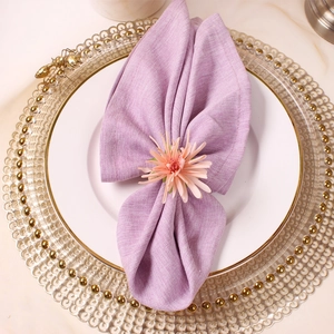 Close-up of pink flower napkin ring on lilac linen fabric with gold decorative plate
