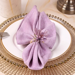 Detail of purple artificial flower napkin ring on soft fabric with gold tableware