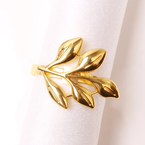 Close-up of golden leaf napkin ring with polished metal finish on a white fabric napkin