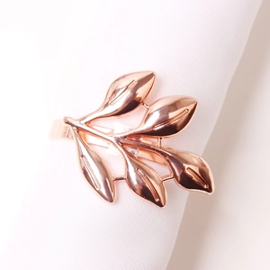 Close-up of polished rose gold leaf napkin ring on a white cloth for table decor