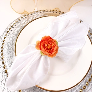 Close-up of orange artificial peony napkin ring on a white textured fabric napkin