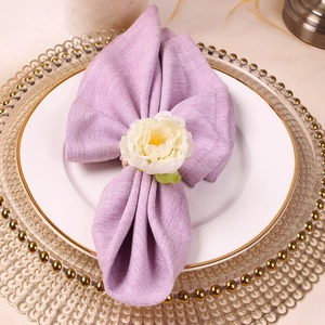 Close-up of white artificial flower napkin ring with purple linen cloth on dinner plate
