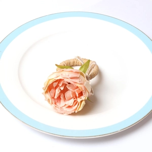 Pink artificial peony flower napkin ring with natural straw band on a white ceramic plate