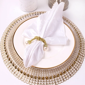 Elegant gold twisted rope napkin ring with pearl accents on a white textured napkin