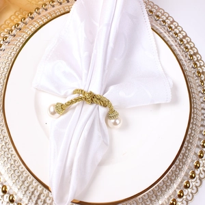 Close-up of golden braided rope napkin ring with white pearls on a white linen napkin