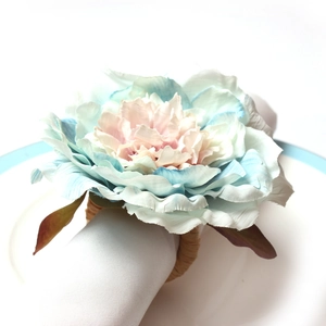 Peony flower napkin ring with vintage blue petals and rustic woven base on a white plate