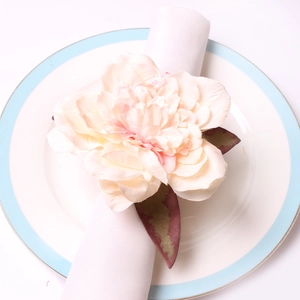 Pink faux peony napkin ring with silk petals and green leaves on a white ceramic plate