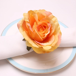 Close-up of artificial peony napkin ring with orange silk petals on a white ceramic plate