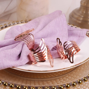 Three-piece rose gold angel wing napkin rings set displayed on a luxury dinner plate