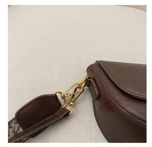 Detail of dark brown leather bag showing golden metal hook and woven geometric strap