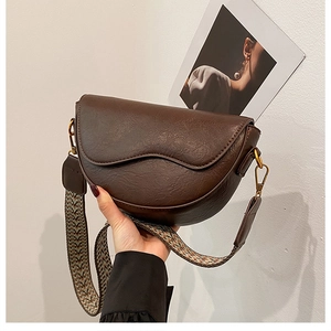 Detail of dark brown saddle bag featuring vintage pebble texture and wide floral woven strap