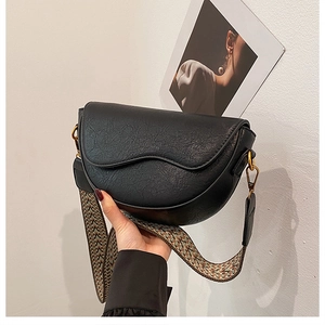 Detail of vintage black saddle bag with cracked leather texture and woven shoulder strap