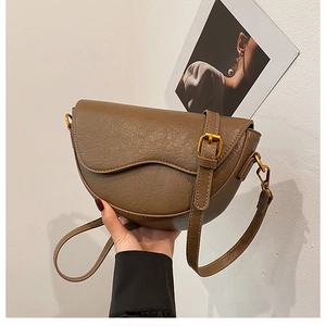 Detail view of the brown textured leather saddle bag with vintage wavy flap and gold buckle