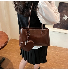 Close-up of a vintage brown leather tote bag with a heart-shaped zipper pouch accessory