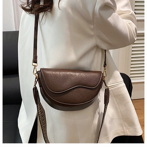 Detail of dark brown saddle bag featuring wave-edge flap and woven shoulder strap