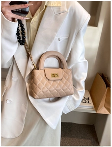 Detail view of beige quilted handbag with gold turn-lock and beaded chain strap