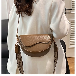 Detailed view of a brown saddle bag featuring lychee texture and woven shoulder strap