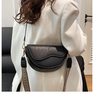 Detail of a black saddle bag with wavy edge and ethnic jacquard strap on white blazer