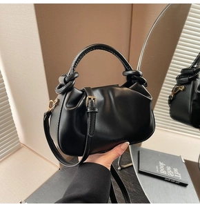Detail of black pleated bucket bag featuring a knotted handle and gold metal hardware