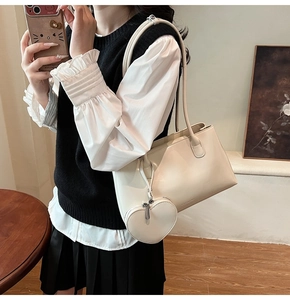 Detail of cream tote bag with heart-shaped charm and adjustable shoulder strap